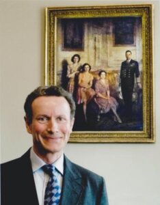 Lord Bruce in a suit and tie standing in front of a painting